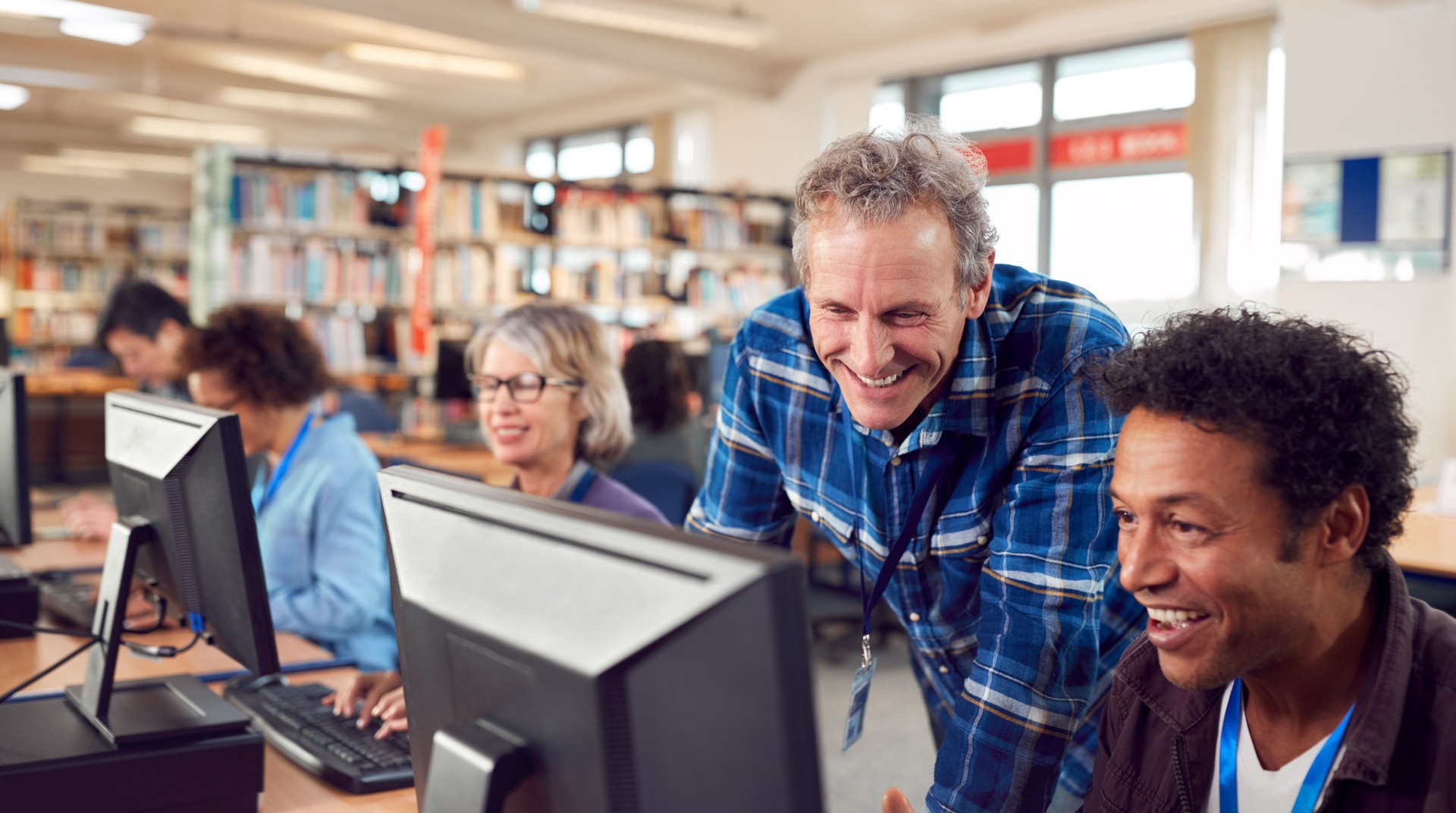 Teacher With Group Of Mature Adult Students In Class Working At Computers In College Library