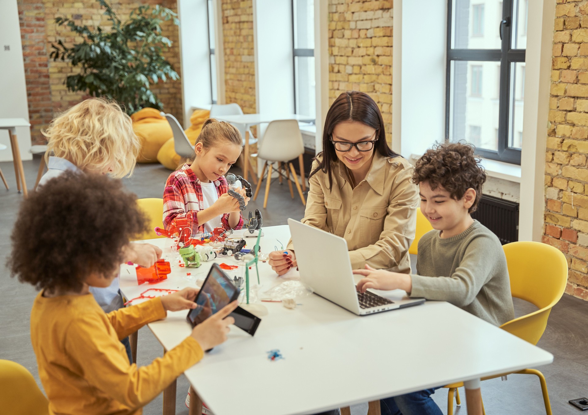 Group of diverse kids working together with young female teacher, sitting at the table during STEM class