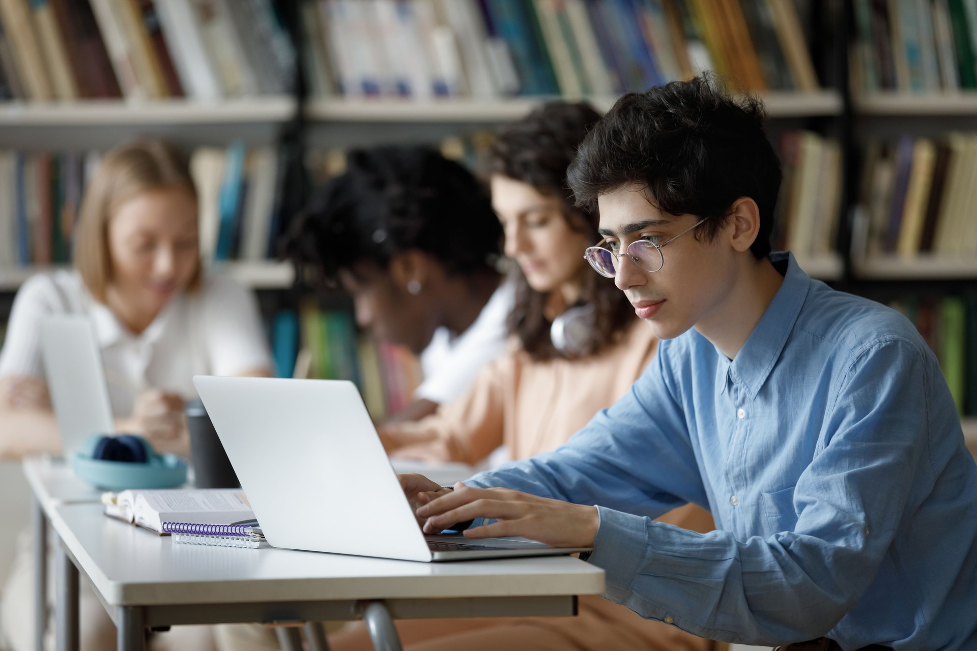 Student guy wear glasses studying in library using laptop